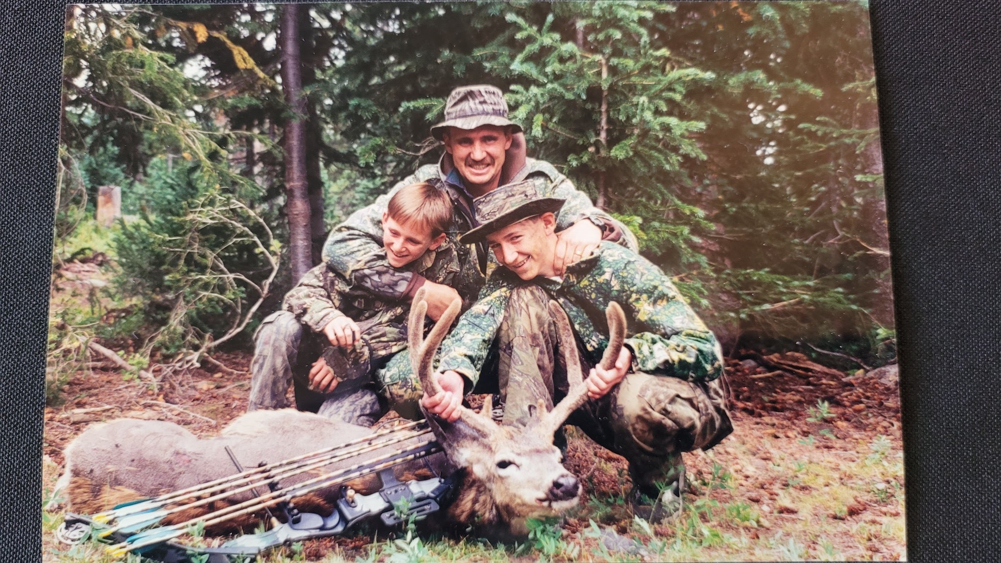 Karl with two of his sons after a bow hunt — deep forest, late afternoon.